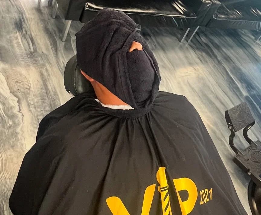 Client reclined under a hot towel wearing a VIP Barber Lounge cape