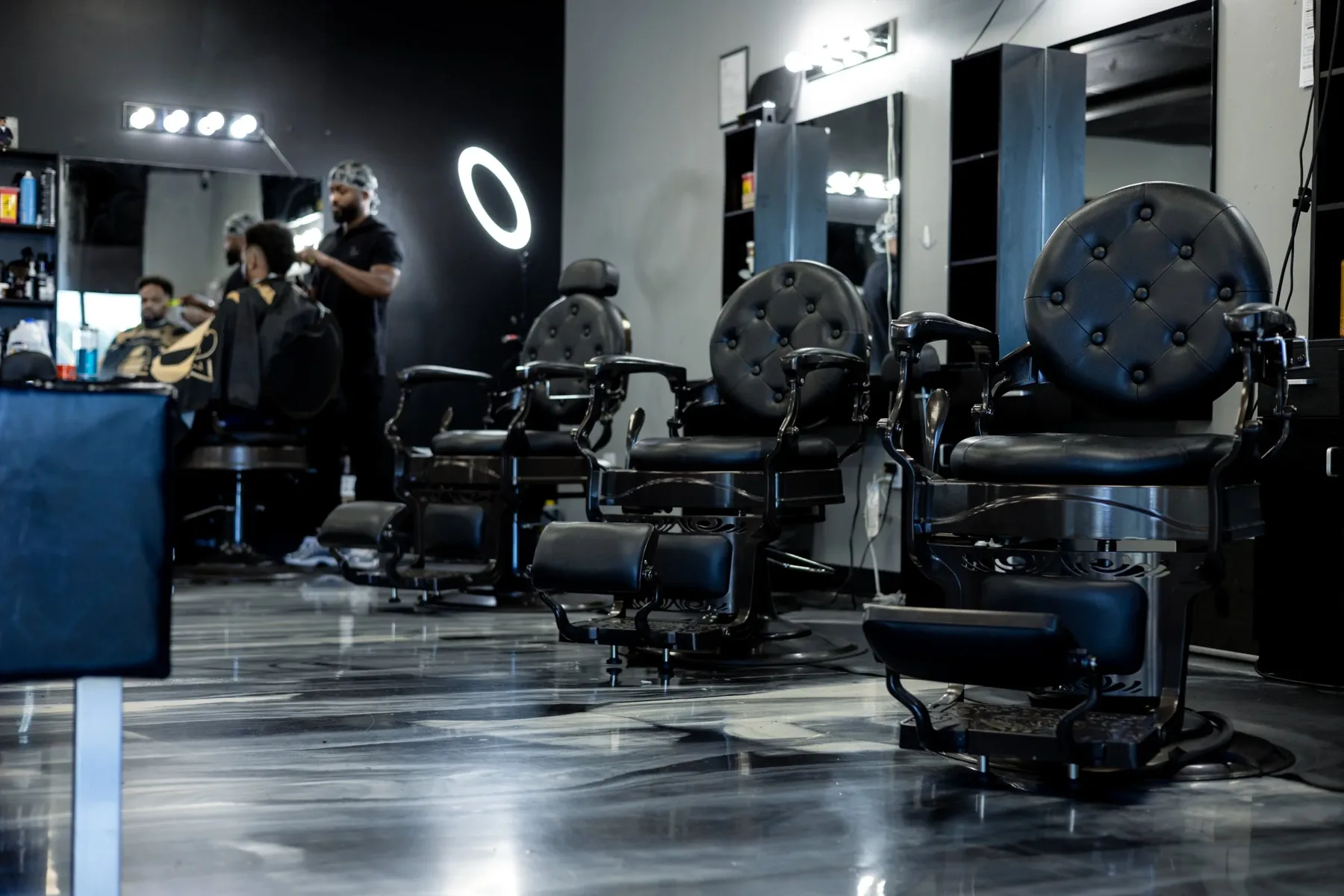 Tufted black barber chairs with a barber cutting a client's hair inside VIP Barber Lounge Aurora