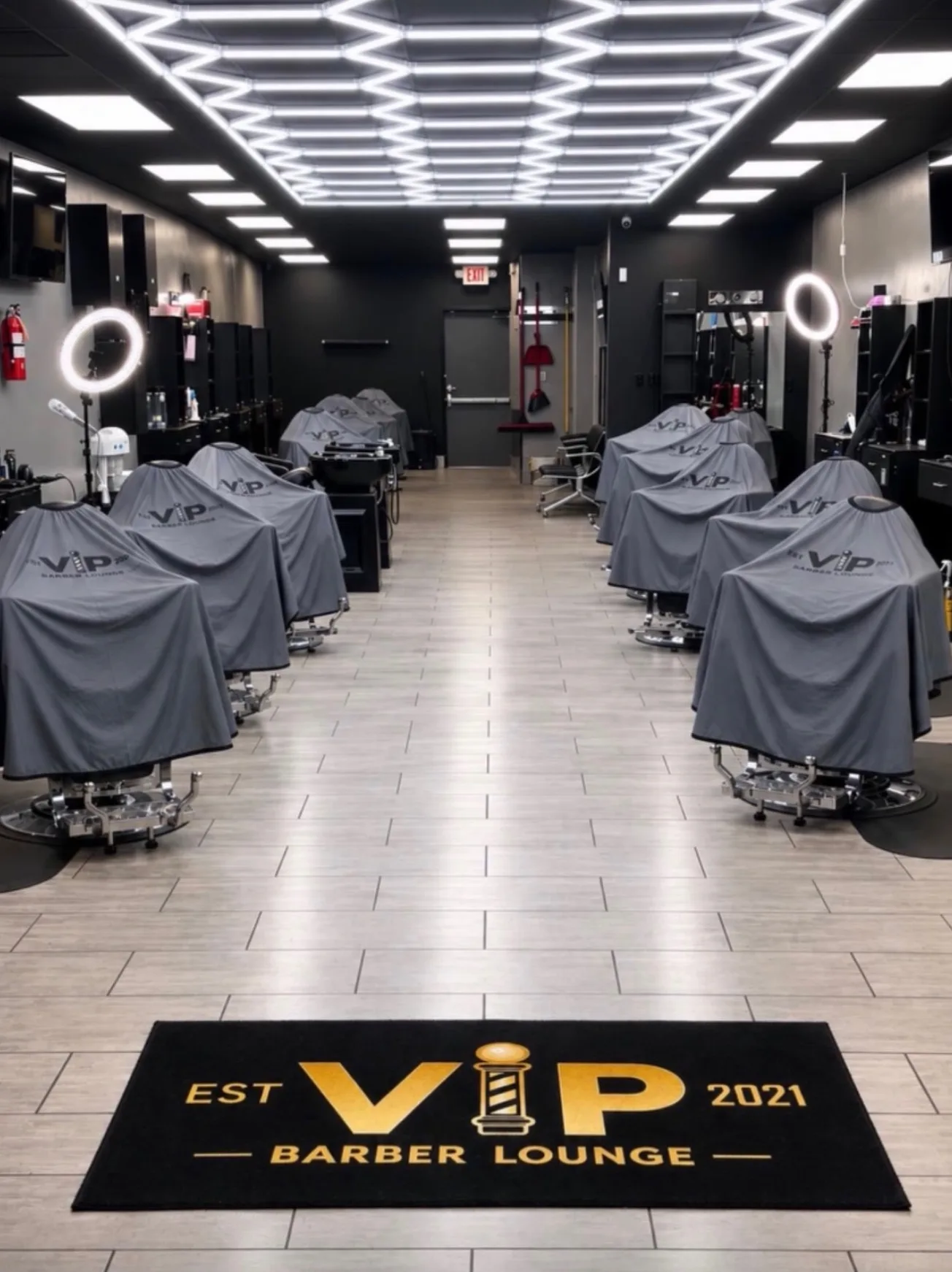 Rows of caped barber chairs under a lit hexagon ceiling inside VIP Barber Lounge Denver